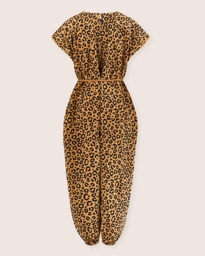 The Rita Tie Back Mini Animal Print Jumpsuit, made from organic cotton, features short sleeves, a cinched waist, elastic ankle hems, and a back zipper closure. It is elegantly displayed on a plain background and boasts a relaxed fit.