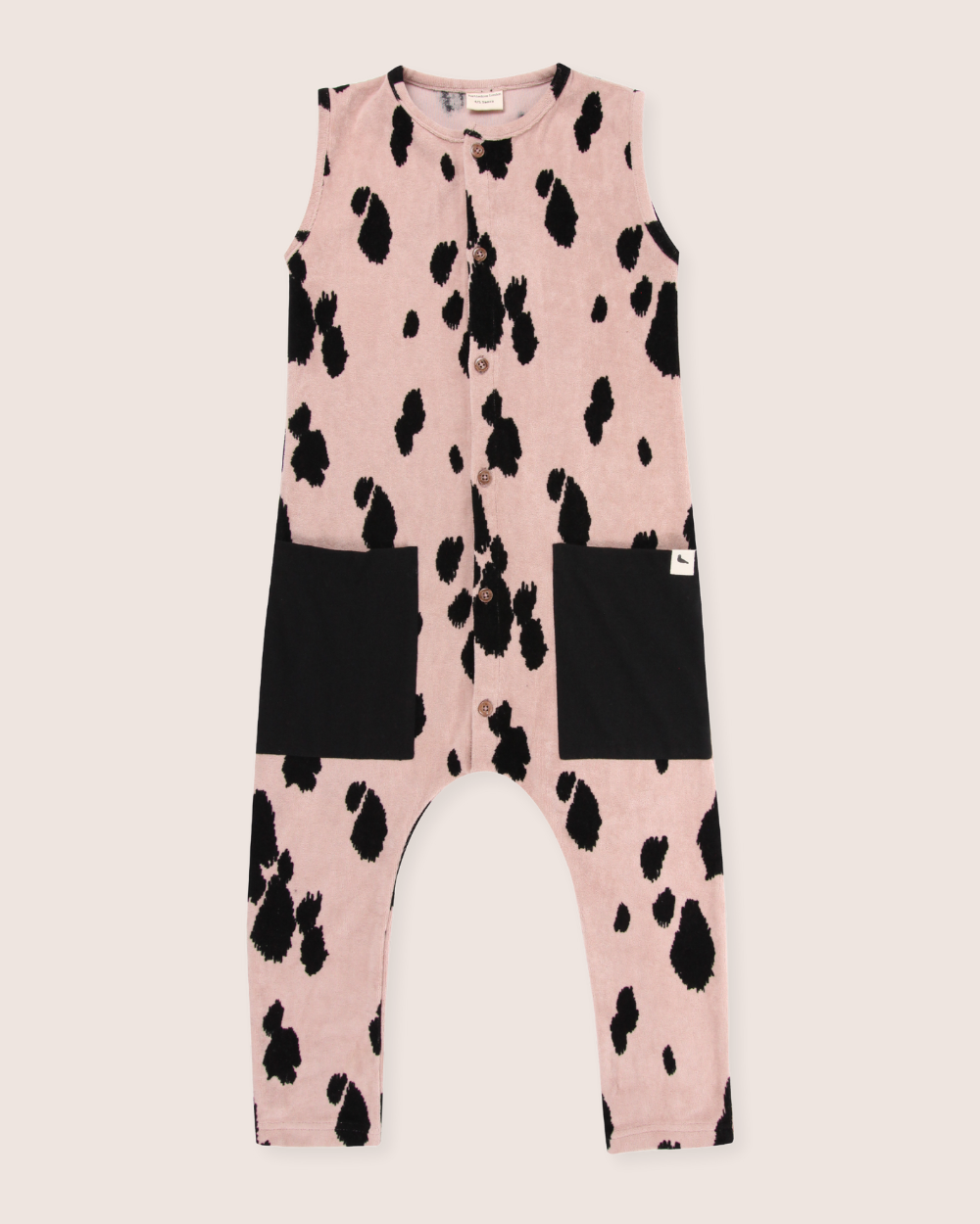 The Pony Velour Dungarees are sleeveless childrens jumpsuits made from organic velour, featuring a pink base with playful black cow spots and two large front black pockets. Ideal for sustainable wardrobes and destined to be a favorite in any kids dungaree collection.