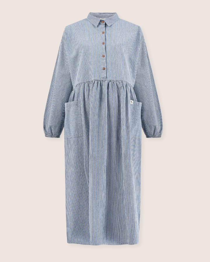 The Magda Pinstripe Denim Dress is a casual, long-sleeved piece in blue and white pinstripe denim. It has a collared neckline, button-down front, gathered waist, large front pockets, and easy breastfeeding access. Made from organic cotton denim.