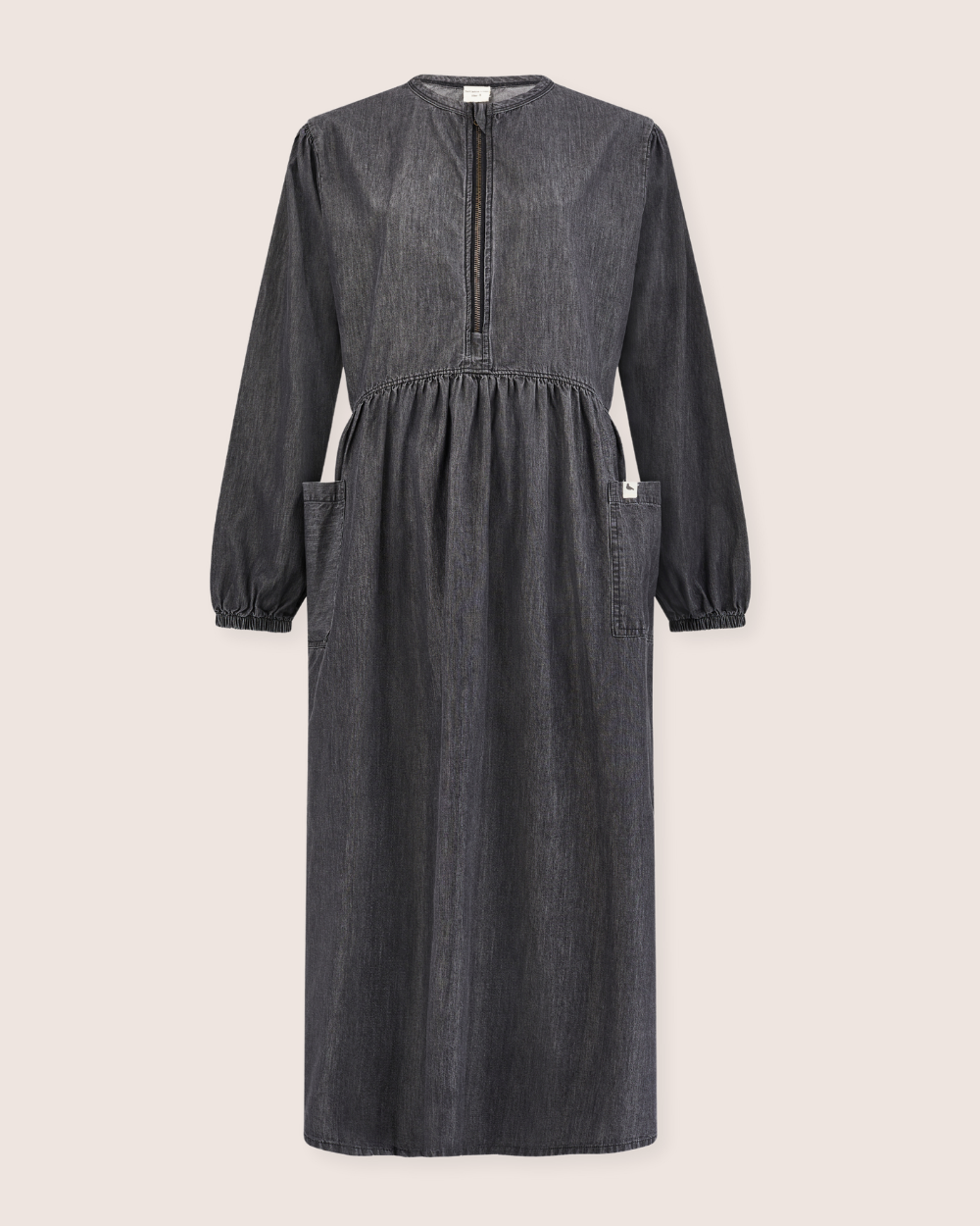 The Magda Black Denim Dress is a long-sleeve, dark denim, midi-length piece crafted from organic cotton. It features a buttoned keyhole neckline for easy breastfeeding access, an elastic waist, two front pockets, and a relaxed fit with the hem falling gracefully below the knees in a minimalist design.