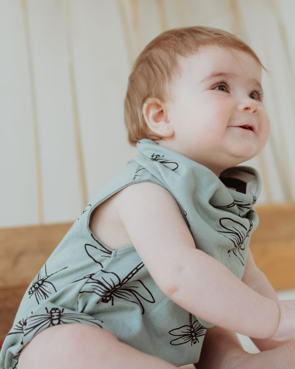 A baby wearing a green bib with black damselfly and stripe print.