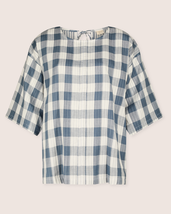 The Doris Tie Back Blue Check Top features blue and white large checkered patterns, a short-sleeve design with a round neckline, crafted from organic cotton for a light and airy feel, ideal for casual wear. Displayed against a plain background.