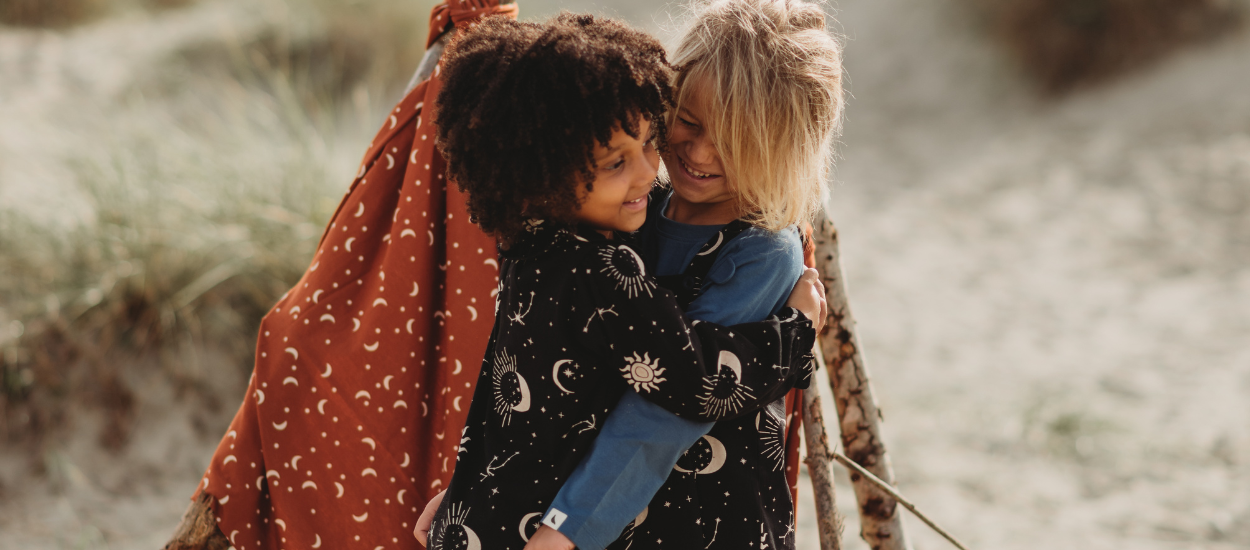 2 children embracing wearing celestial dress and dungarees 