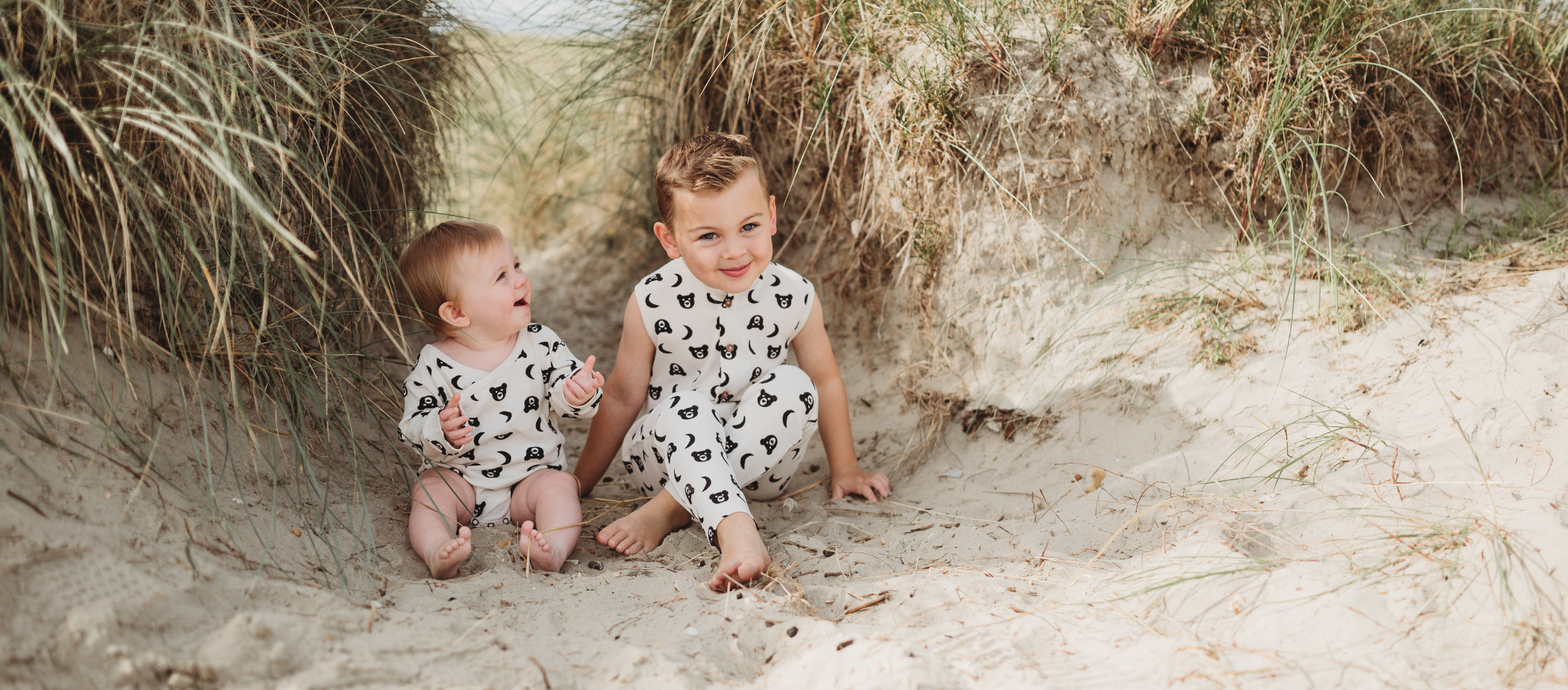 2 kids sitting on beach wearing bear print all in ones 