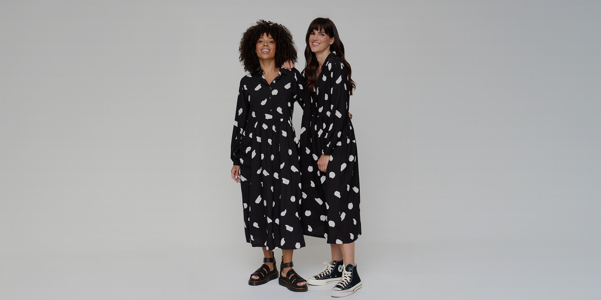 Two women wearing matching black dresses with white patterns on a gray background