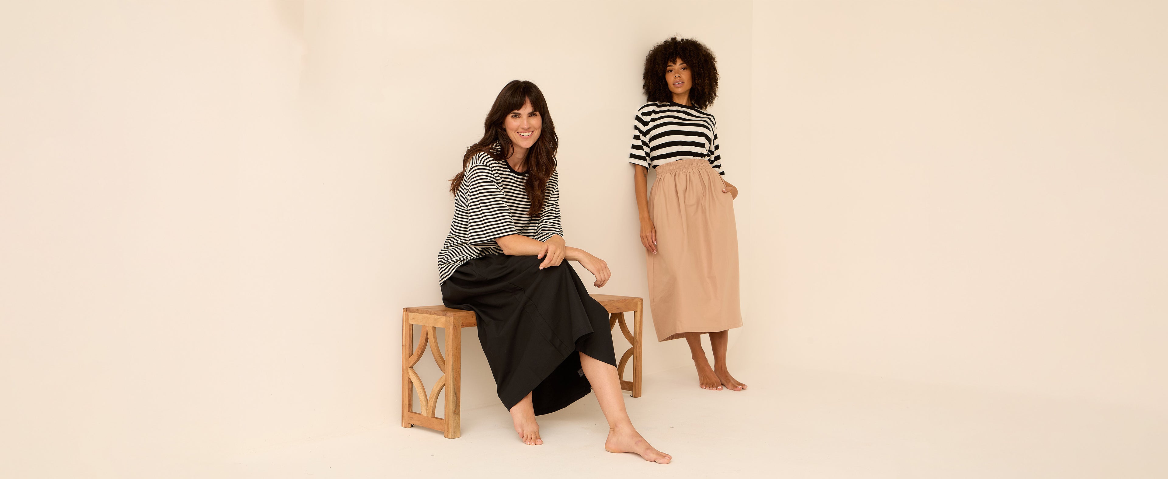 2 women standing side by side. one wearing stripe elsie tshirt and black joyce skirt. the other wearing beige joyce skirt and monochrome stripe tee 