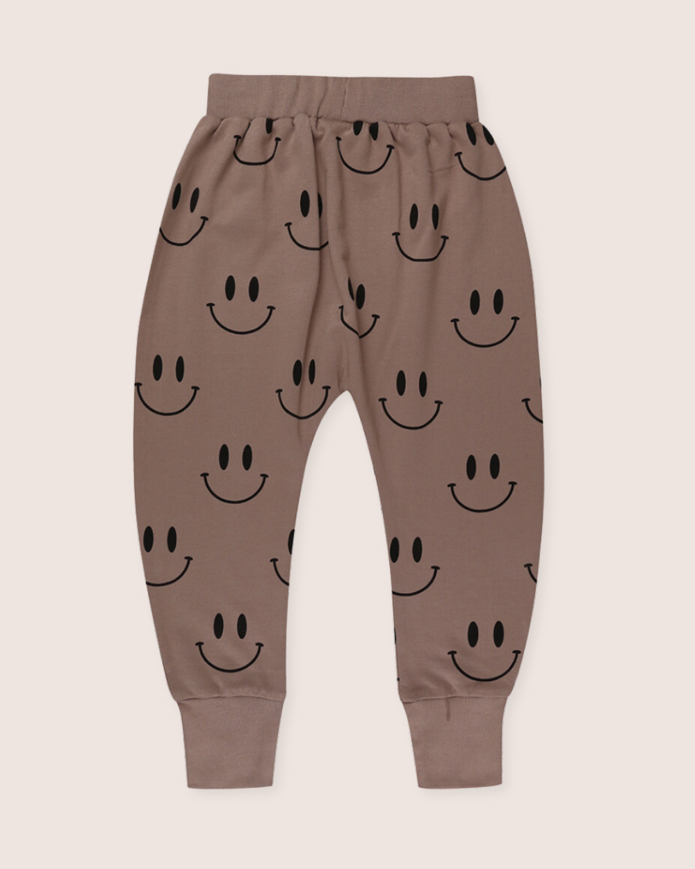 The Smiley Harems are brown kids joggers made from organic cotton, featuring an elastic waistband and cuffs with a playful smiley face print on a light, neutral background.