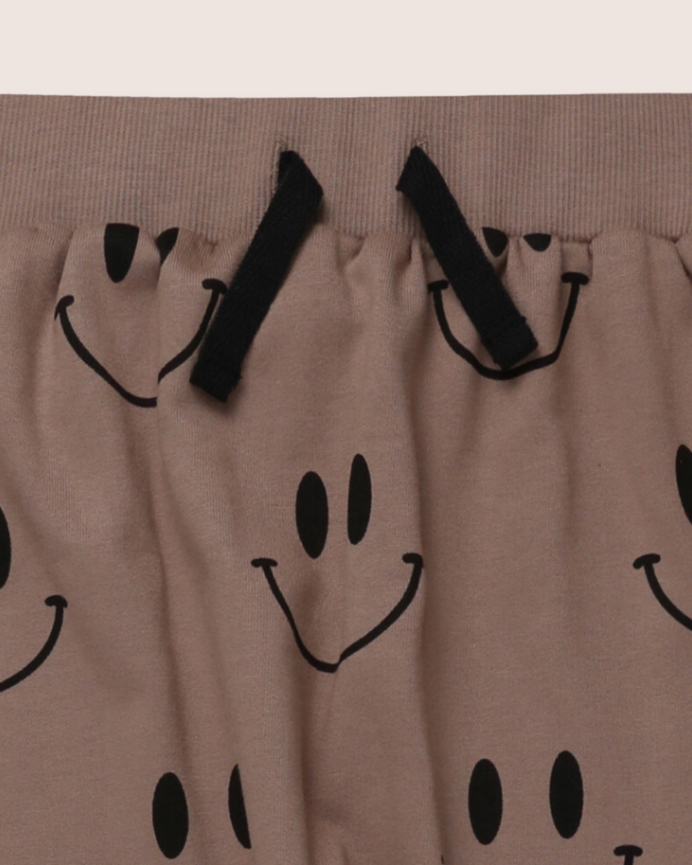 The Smiley Harems are kids joggers made from soft organic cotton in light brown fabric, featuring playful black Smiley Face prints. They have black drawstrings and an elastic waistband for a comfortable, casual fit.