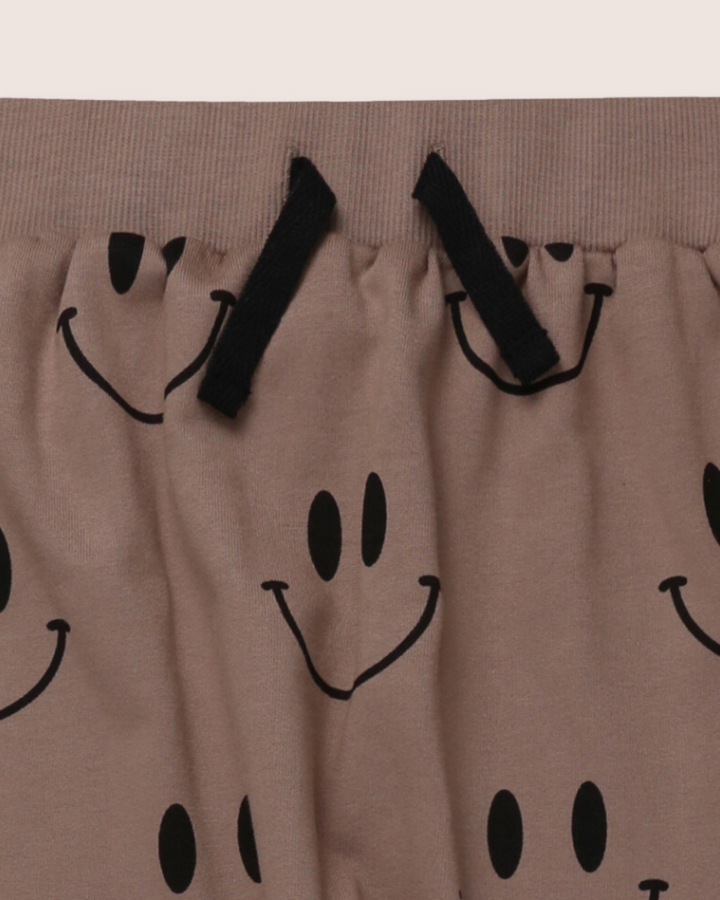 The Smiley Harems are kids joggers made from soft organic cotton in light brown fabric, featuring playful black Smiley Face prints. They have black drawstrings and an elastic waistband for a comfortable, casual fit.