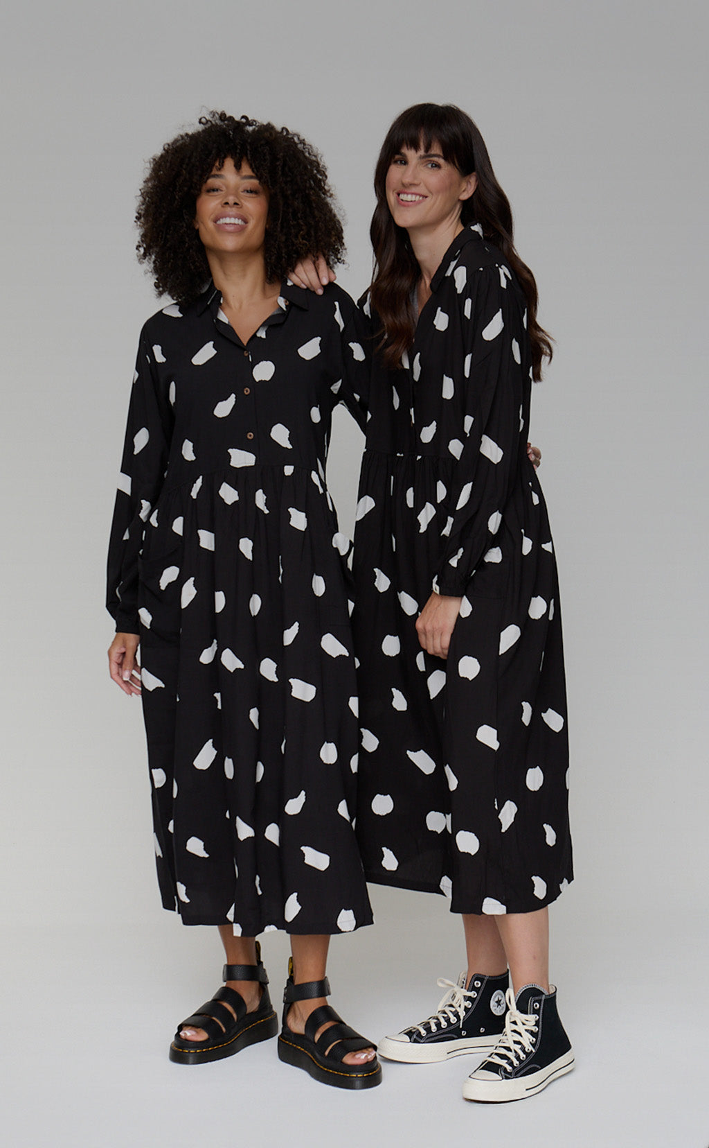 Two women wearing black dresses with white patterns against a gray background