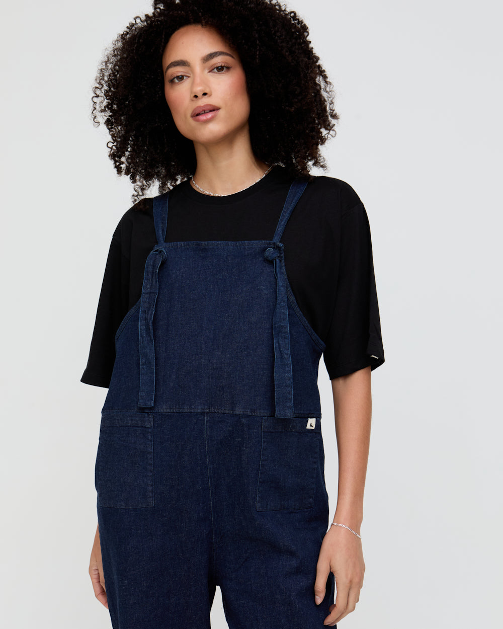 Person wearing blue denim overalls over a black top on a plain background