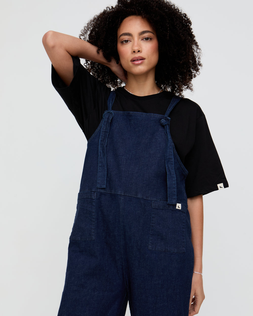 Person wearing blue denim overalls over a black top on a plain background