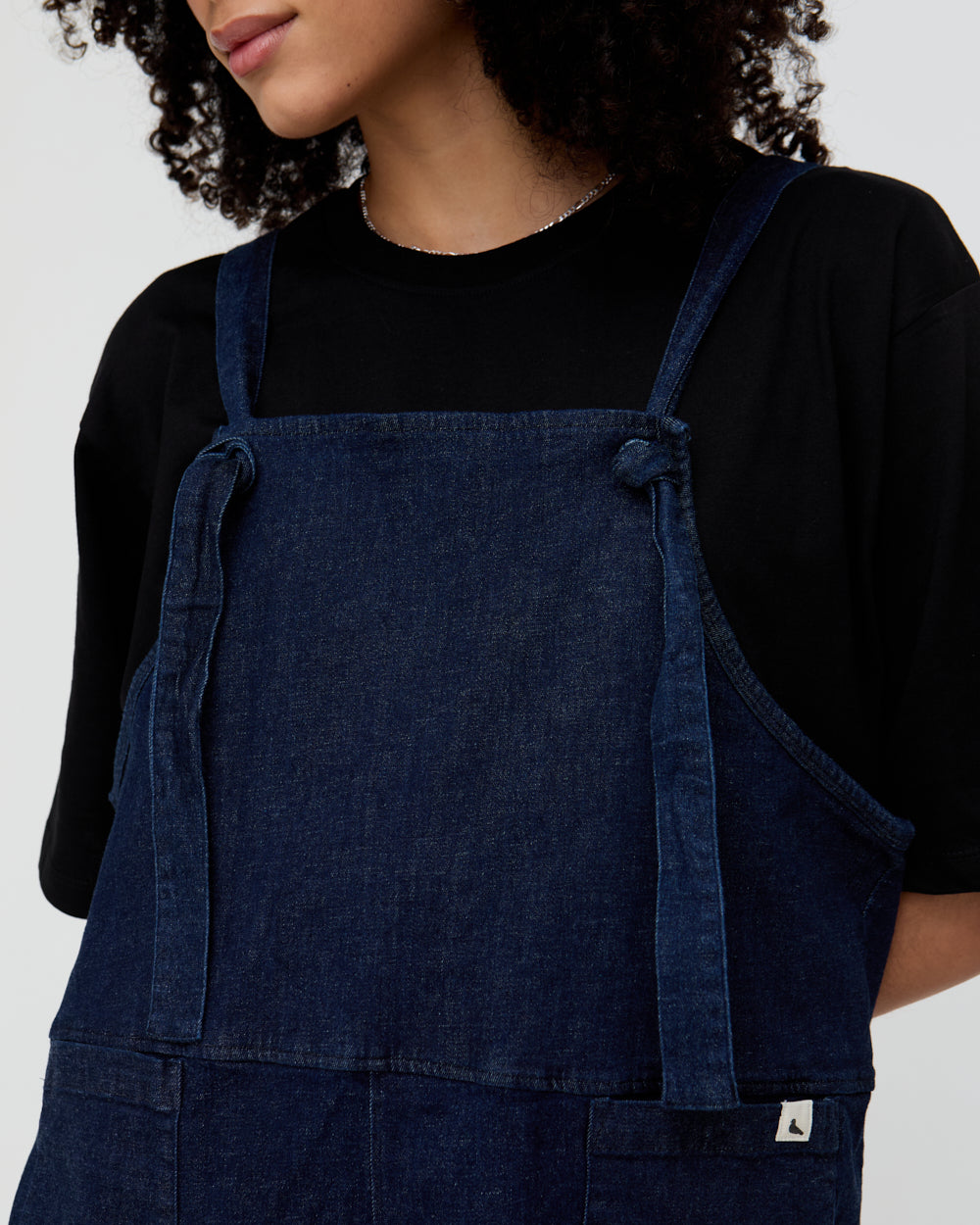Person wearing a blue denim apron over a black shirt on a white background