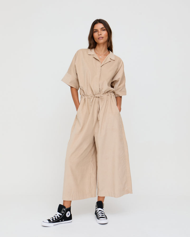 Woman wearing a beige jumpsuit with a white background