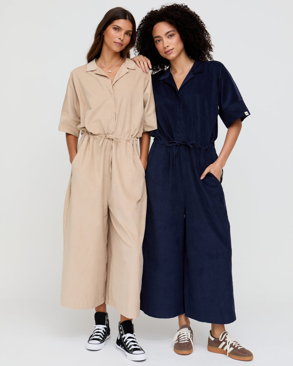 Two women wearing beige and navy jumpsuits on a white background