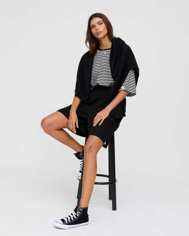 Woman sitting on a stool wearing a black outfit with a striped shirt against a white background