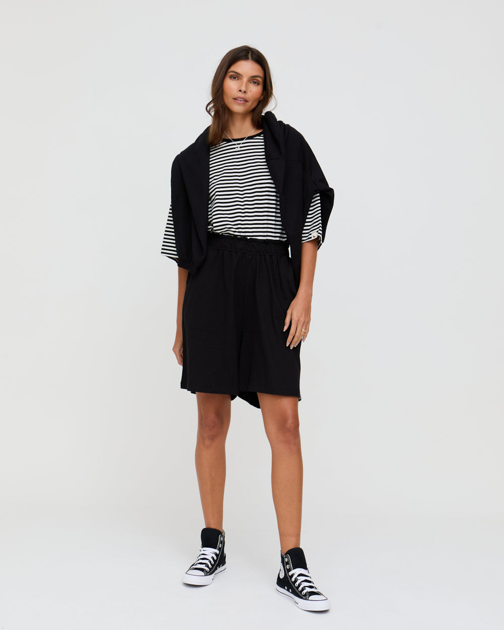 Woman wearing a black and white striped top with a black cardigan and shorts on a white background