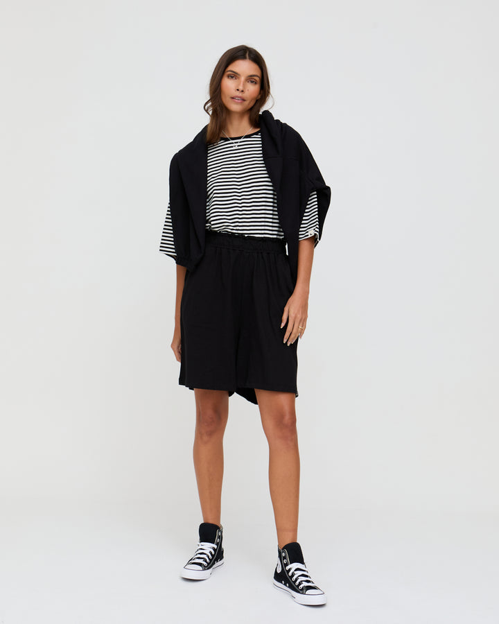 Woman wearing a black and white striped top with a black cardigan and shorts on a white background