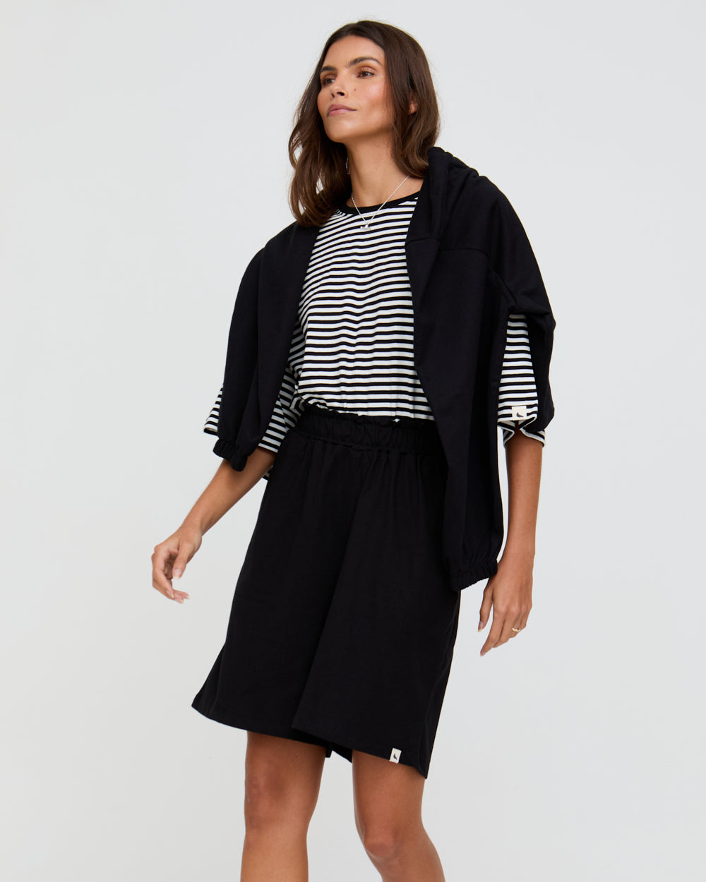 Woman wearing a black jacket, striped shirt, and black skirt on a white background