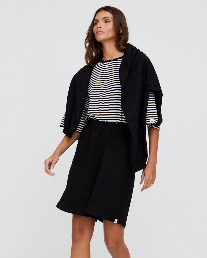 Woman wearing a black jacket, striped shirt, and black skirt on a white background