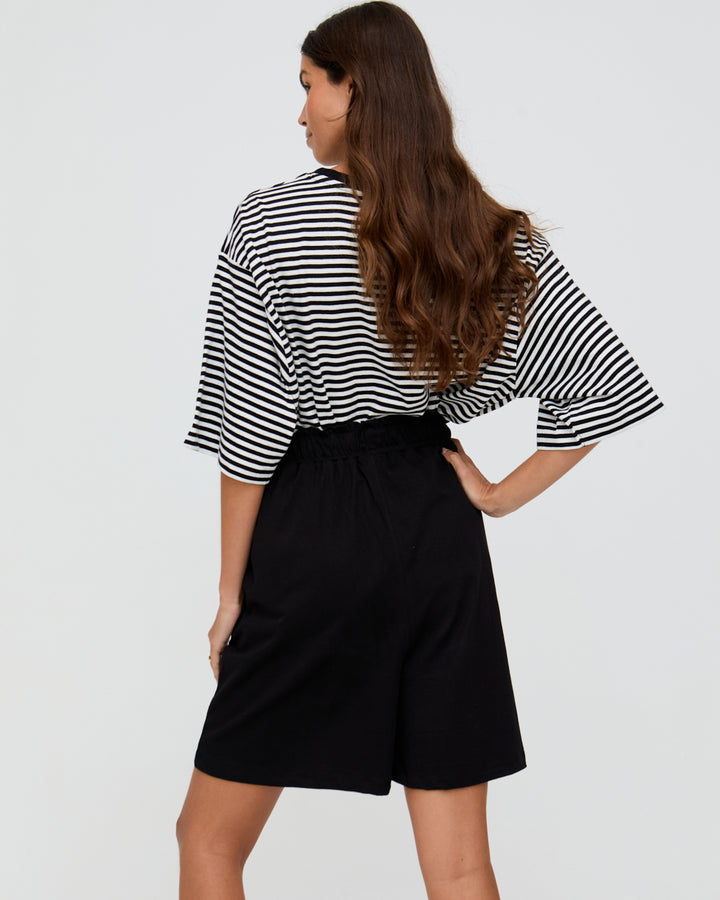 Woman wearing a black and white striped shirt and black shorts on a plain background