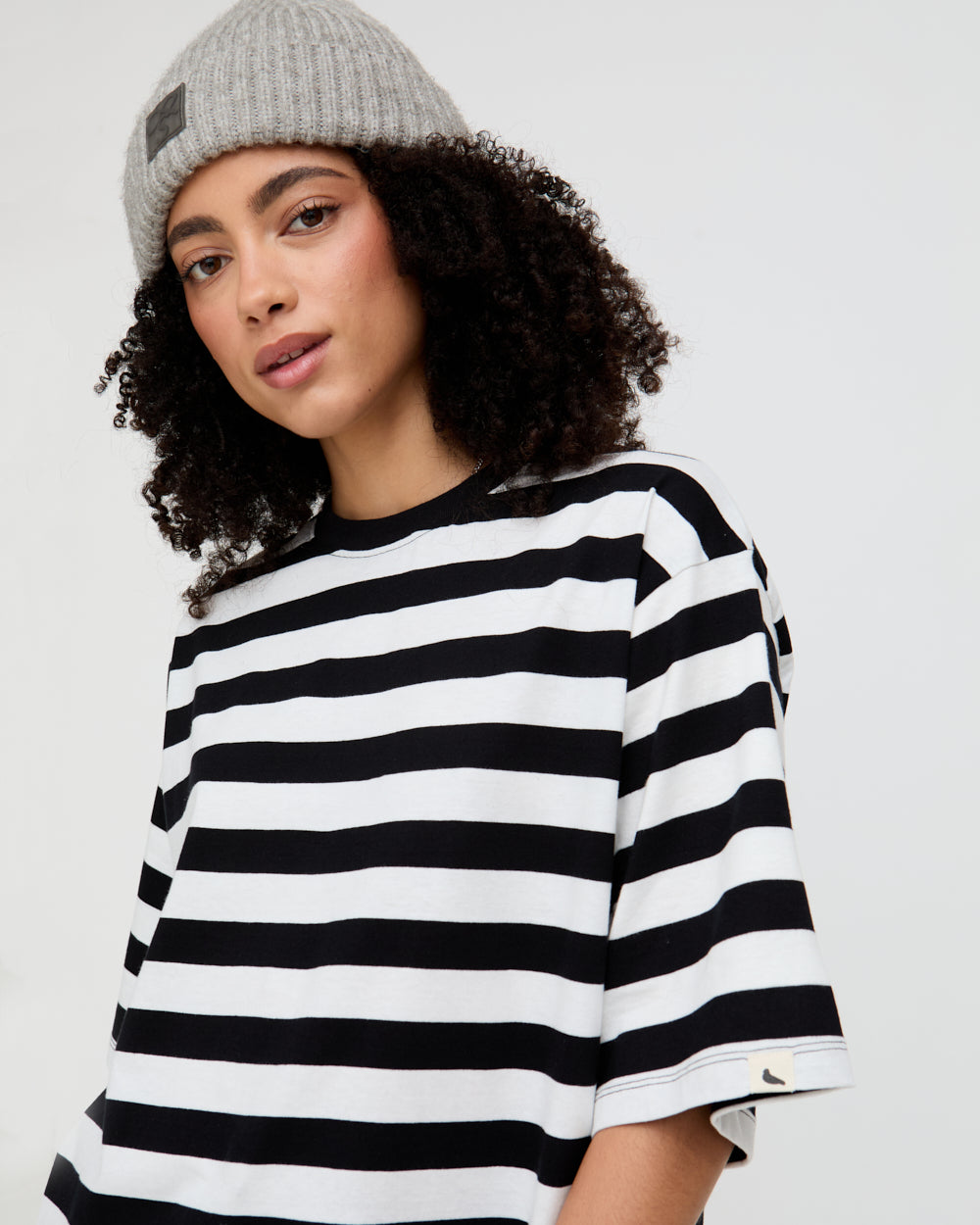 Person wearing a black and white striped shirt and gray beanie on a plain background